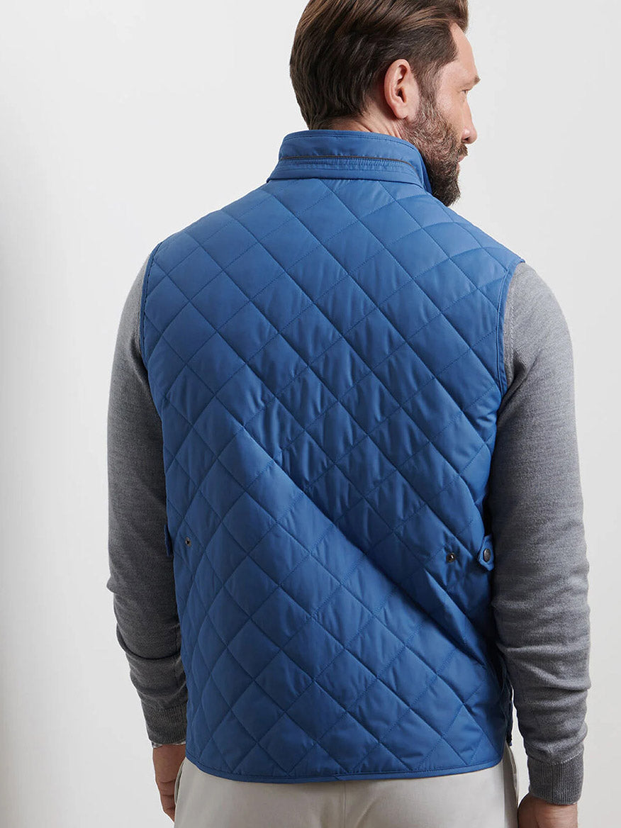 A man wearing a Peter Millar Essex Vest in Astral Blue over a gray long-sleeve shirt stands facing away from the camera.
