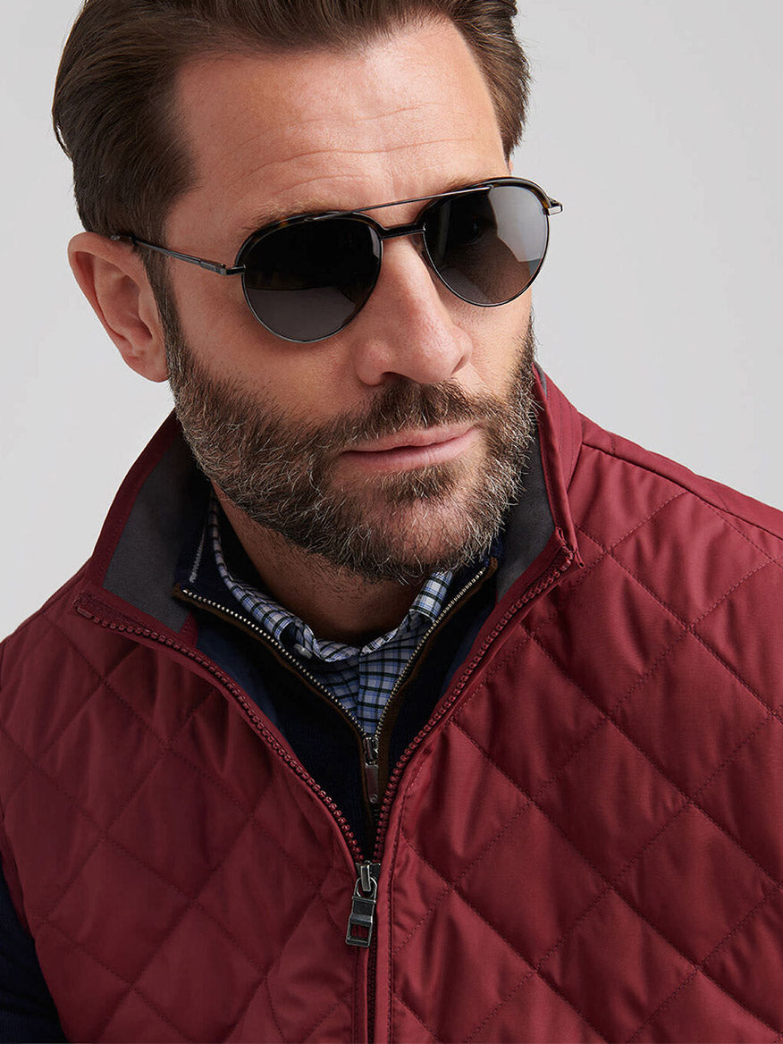 Man with brown hair and beard wearing black sunglasses and a Peter Millar Essex Vest in Autumn Foliage over a blue checkered shirt, looking slightly to the side.