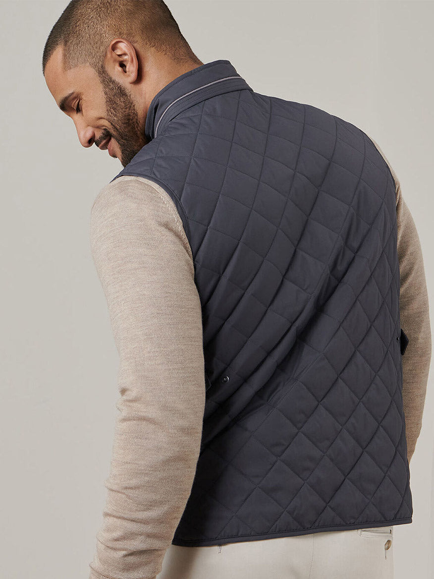 A man facing away wears a Peter Millar Essex Vest in Iron over a beige long-sleeve shirt, standing against a plain light background.