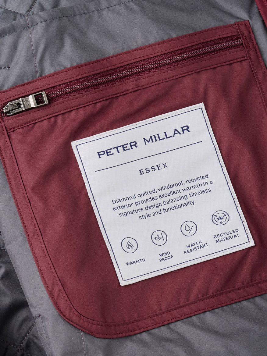 Close-up of the maroon interior jacket pocket with a zipper and a white Peter Millar Essex label, showcasing features like warmth, windproof and water-resistant protection, recycled materials, and the quilted vest construction—all part of the Peter Millar Essex Vest in Bordeaux designed for exceptional comfort in any condition.