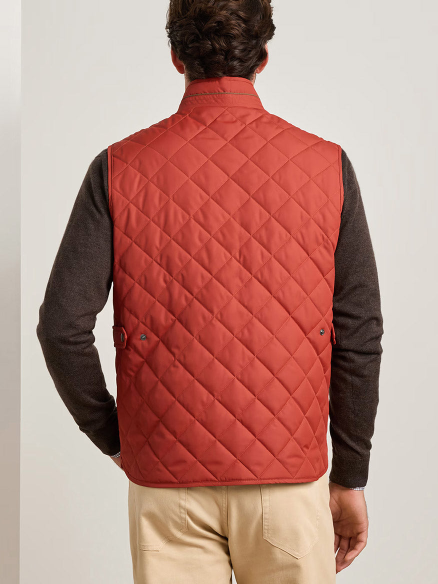 A man shown from the back wearing the Peter Millar Essex Vest in Burnt Orange over a dark long-sleeve shirt and beige pants.