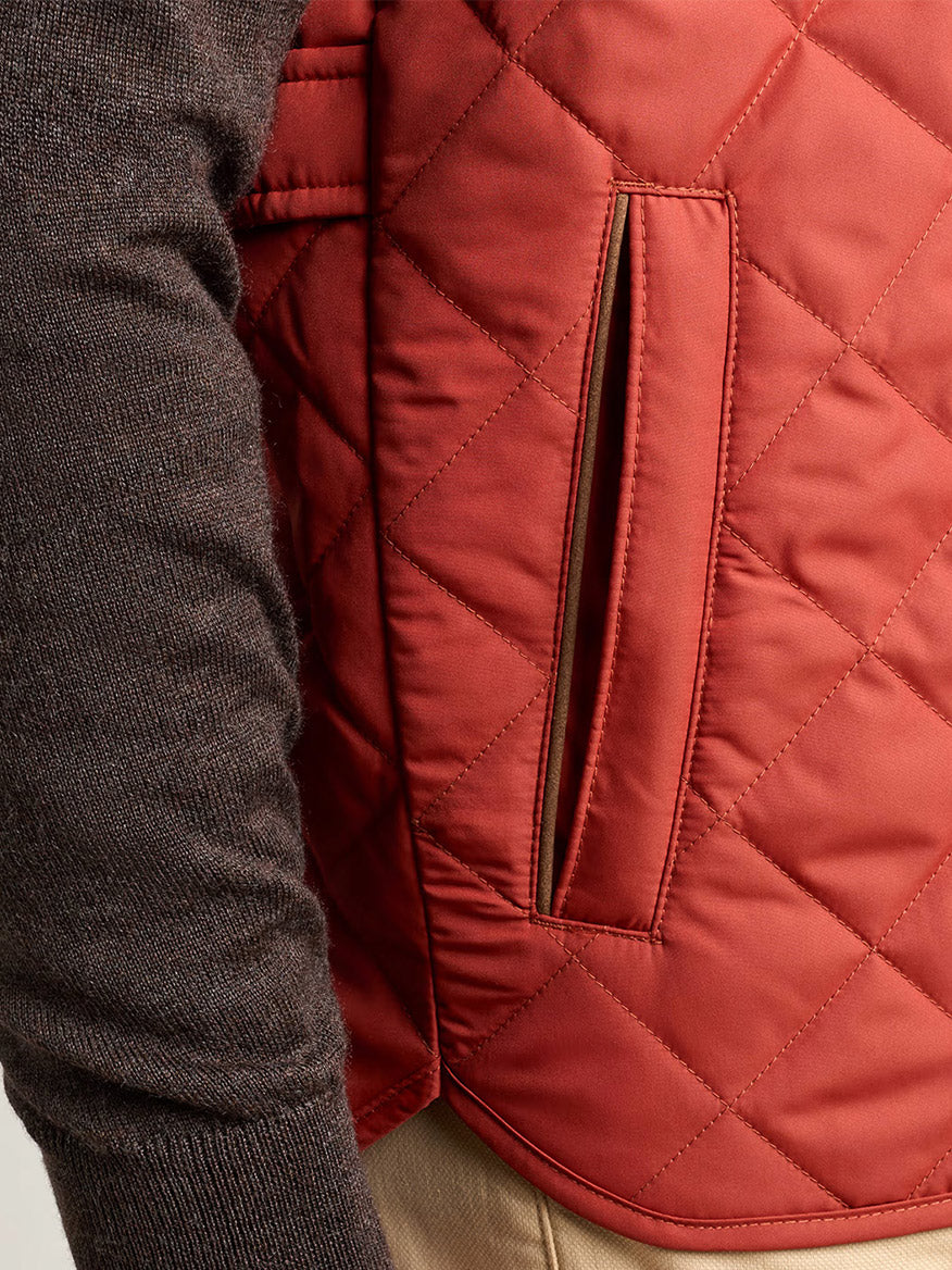 Close-up of a person wearing a brown long-sleeve shirt, tan pants, and the Peter Millar Essex Vest in Burnt Orange, featuring a visible side pocket.