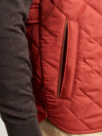Close-up of a person wearing a brown long-sleeve shirt, tan pants, and the Peter Millar Essex Vest in Burnt Orange, featuring a visible side pocket.