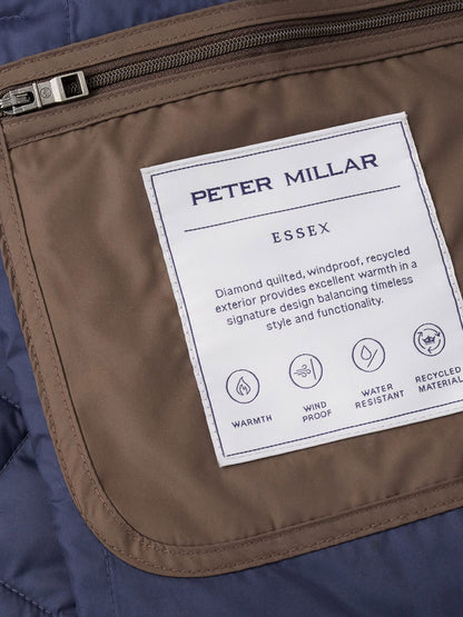 Close-up of a brown quilted vest pocket with a white label that reads “Peter Millar Essex Vest in French Press” and details the vest’s warmth, windproof and water-resistant properties, as well as its use of recycled materials.