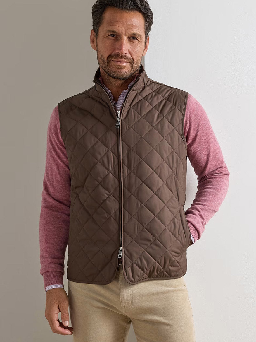 Man wearing the Peter Millar Essex Vest in French Press over a pink long-sleeve shirt and beige pants, standing against a plain light background.