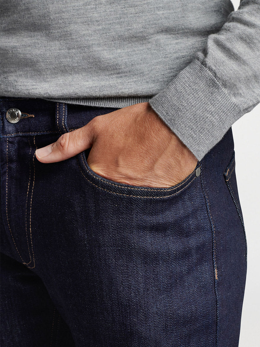 A person inserting their hand into the front pocket of their blue jeans, underneath a Peter Millar Excursionist Flex Crew in Gale Grey.