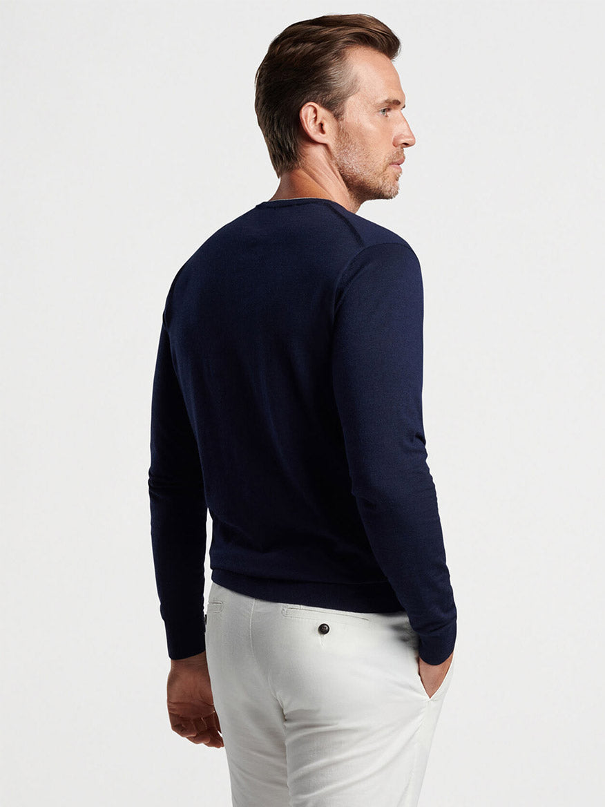 Man in a Peter Millar Excursionist Flex Crew in Navy sweater and white pants standing sideways.