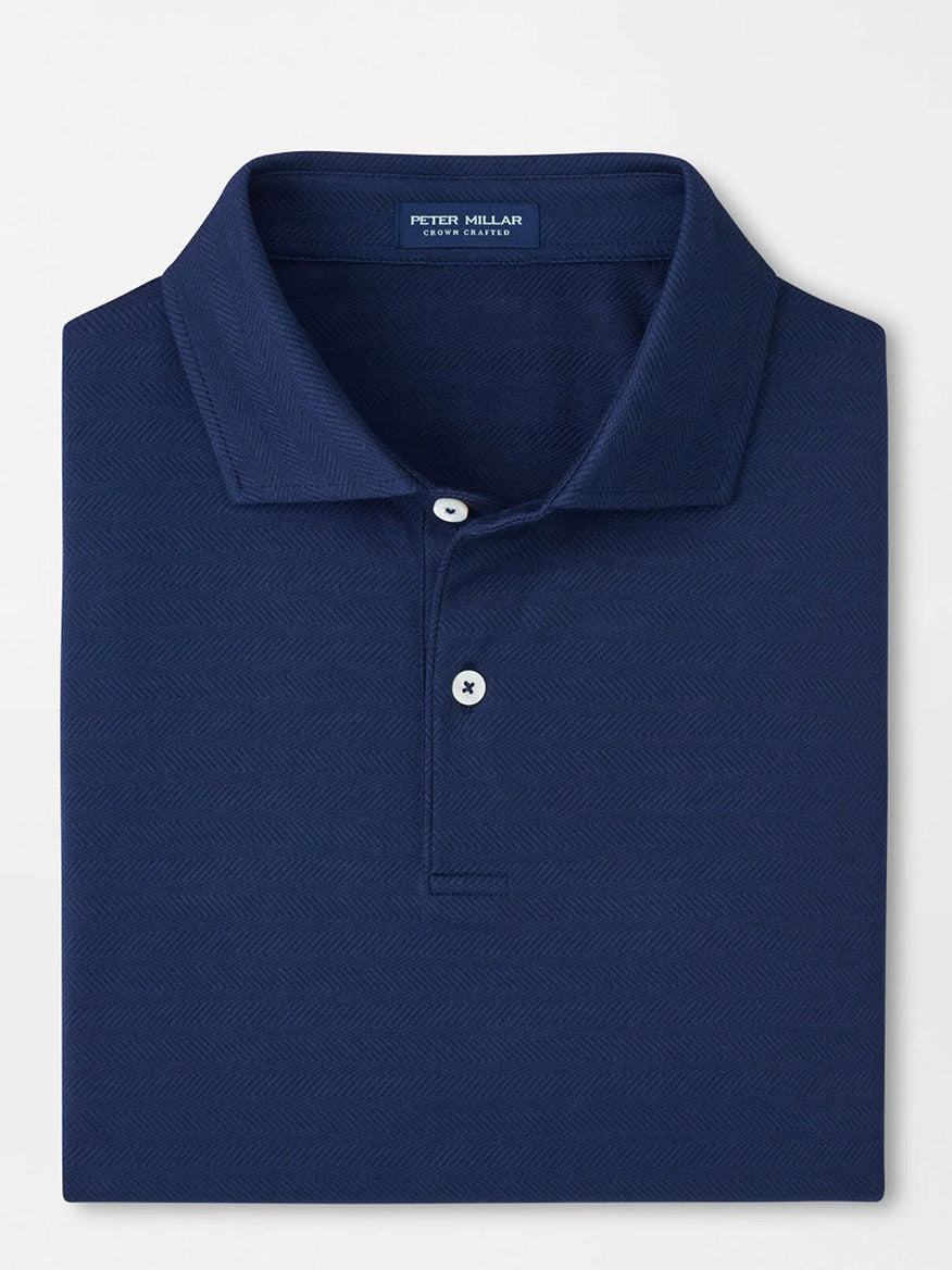 A neatly folded Peter Millar Excursionist Flex Herringbone Knit Polo in Navy features a collared design, two white buttons, and the brand label inside the neckline, crafted from soft cotton jersey knit for comfort.