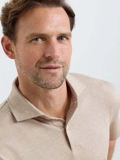 A man with short brown hair and light stubble wears the Peter Millar Excursionist Flex Herringbone Knit Polo in Truffle, facing the camera against a plain light background.