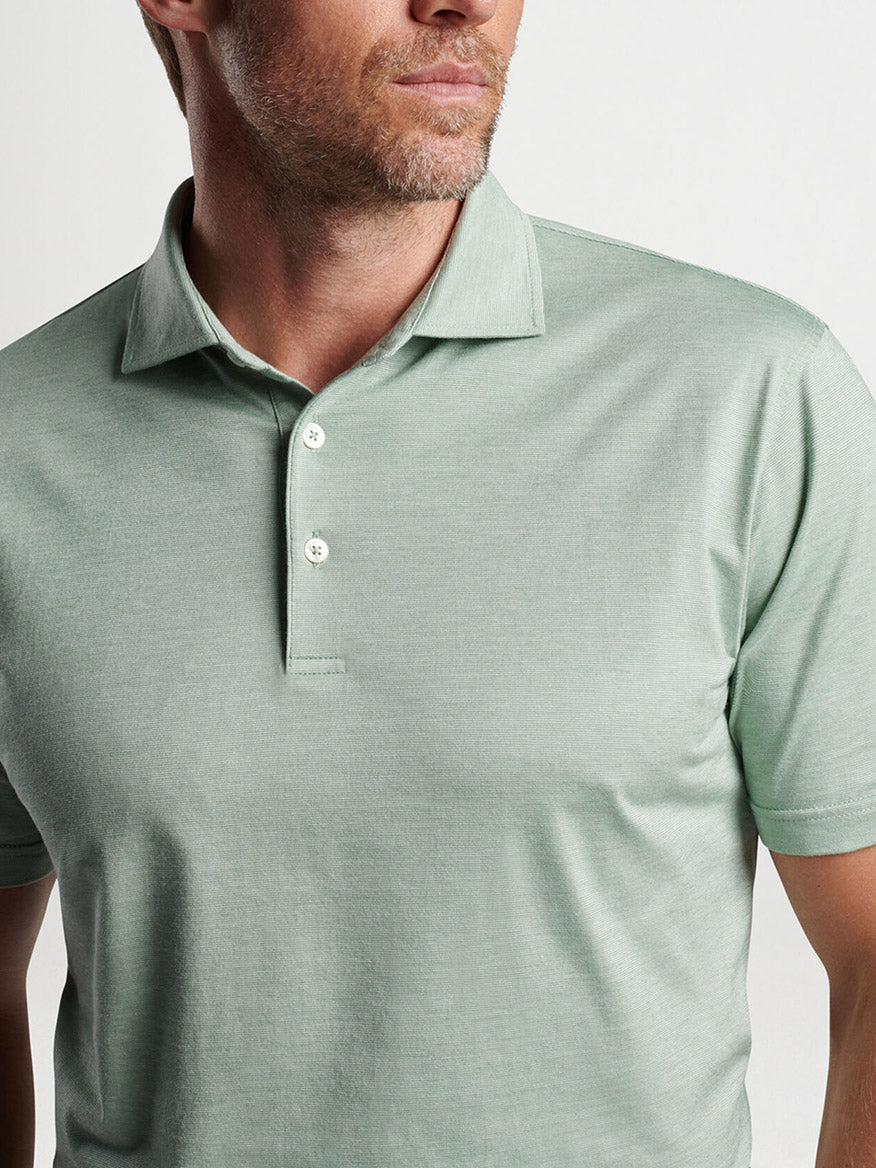 A man wearing a green Peter Millar Excursionist Flex Short-Sleeve Polo in Sage Fog, showcasing a refined casual style.