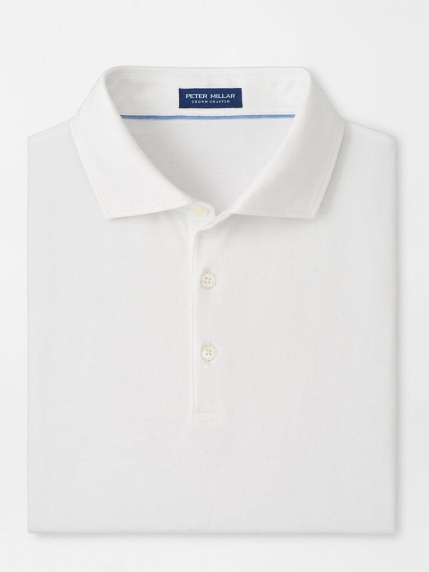 The Peter Millar Excursionist Flex Polo in White is a folded, cotton-based jersey knit polo with a collar and three buttons. A blue label inside the collar displays "Peter Millar.