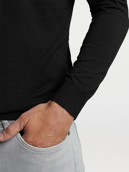 A person with their hand in the pocket of light gray trousers, wearing a luxury black Peter Millar Excursionist Flex Popover Hoodie in Black.