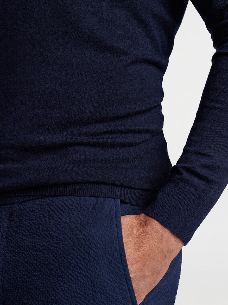 Close-up view of a person wearing a Peter Millar Excursionist Flex Popover Hoodie in Navy and matching pants made from performance yarn with one hand in their pocket.