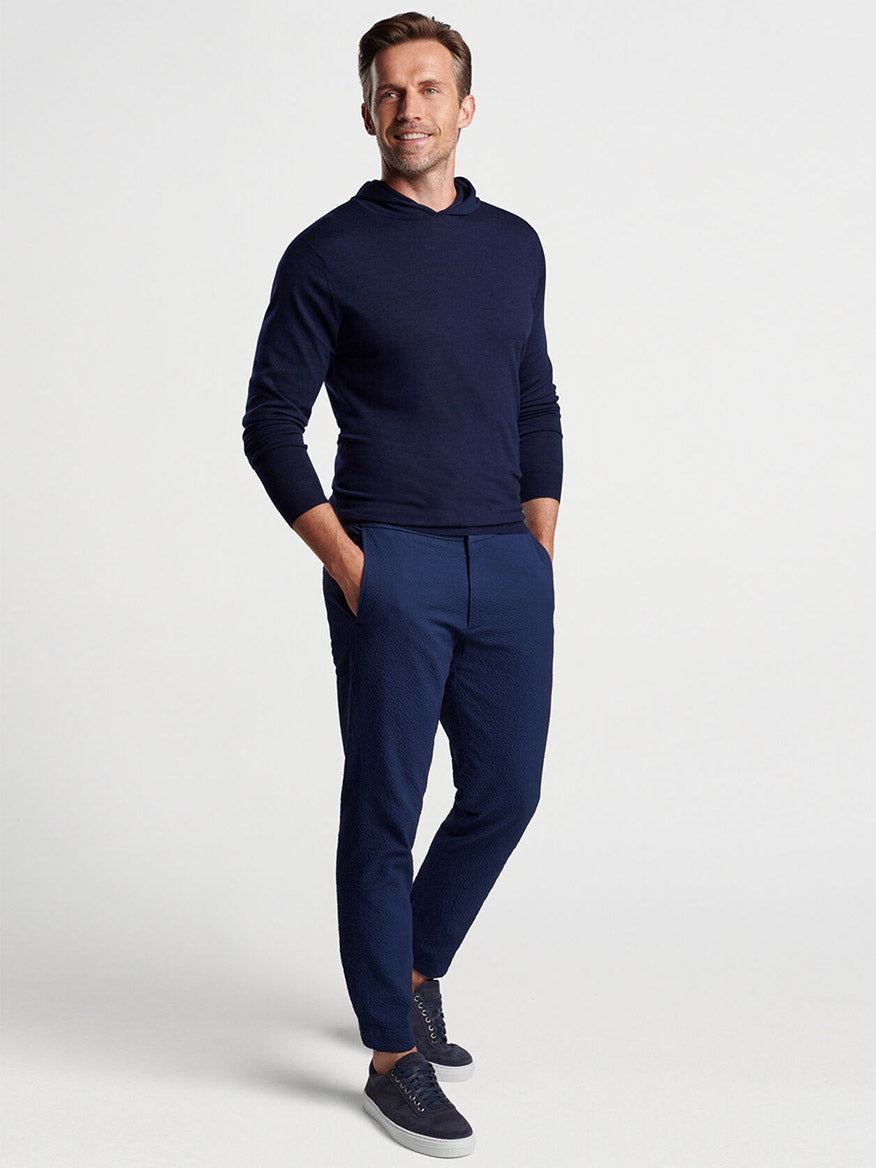 Man in a casual navy blue Peter Millar Excursionist Flex Popover Hoodie and pants with hands in pockets posing for a luxury fashion display.