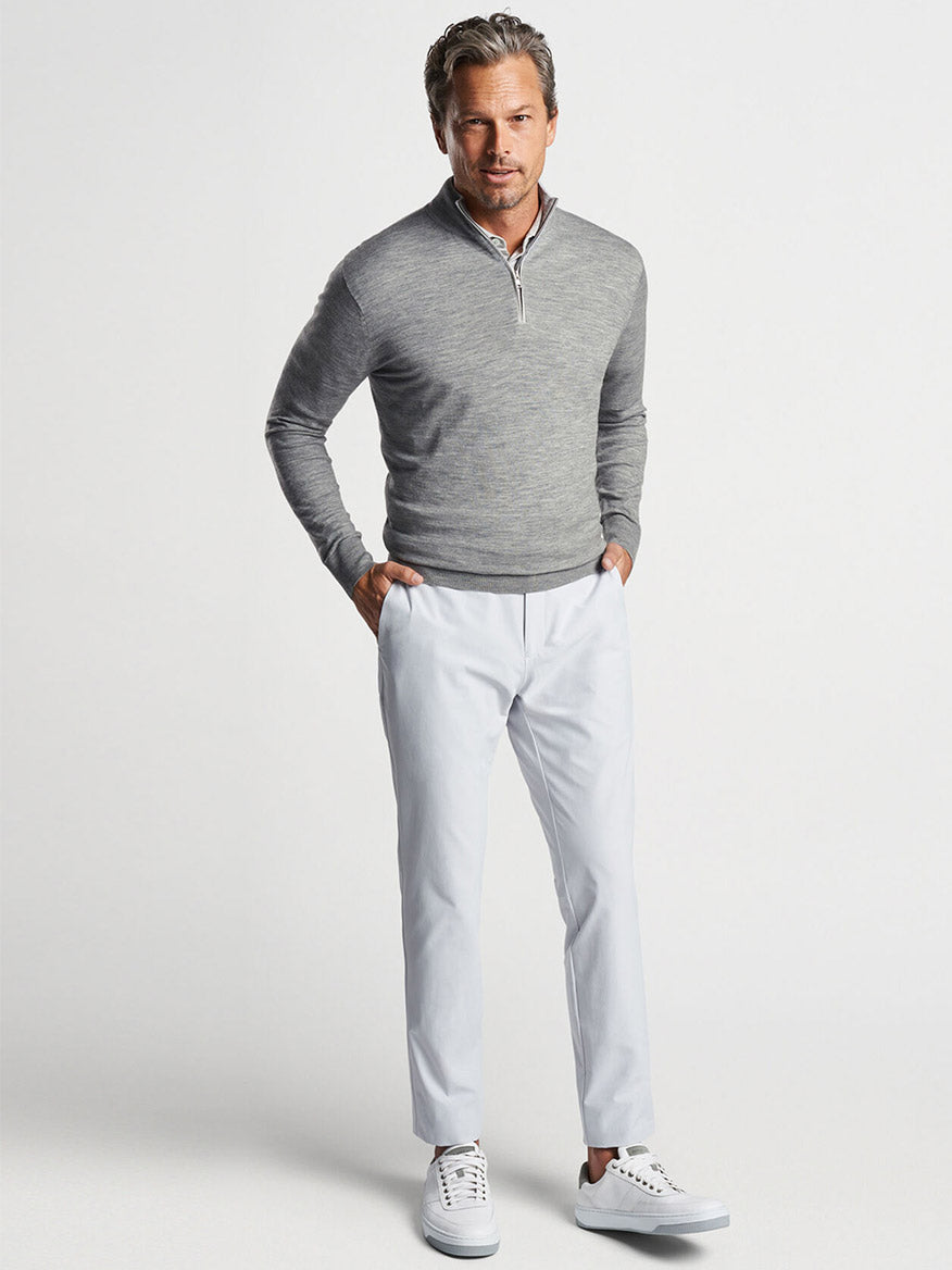 Man posing in a Peter Millar Excursionist Flex Quarter-Zip in Gale Grey, white pants, and casual white sneakers.