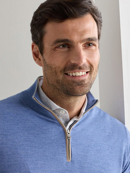 A man with short brown hair and light stubble is smiling, wearing the Peter Millar Excursionist Flex Quarter-Zip Sweater in Navy over a collared shirt, standing indoors.