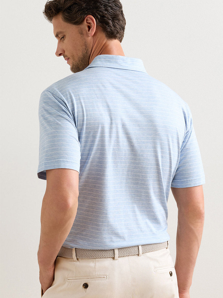 Man facing away, wearing a Peter Millar Excursionist Flex Striped Polo in Blue Frost made from soft cotton jersey knit, paired with beige pants and a light belt.