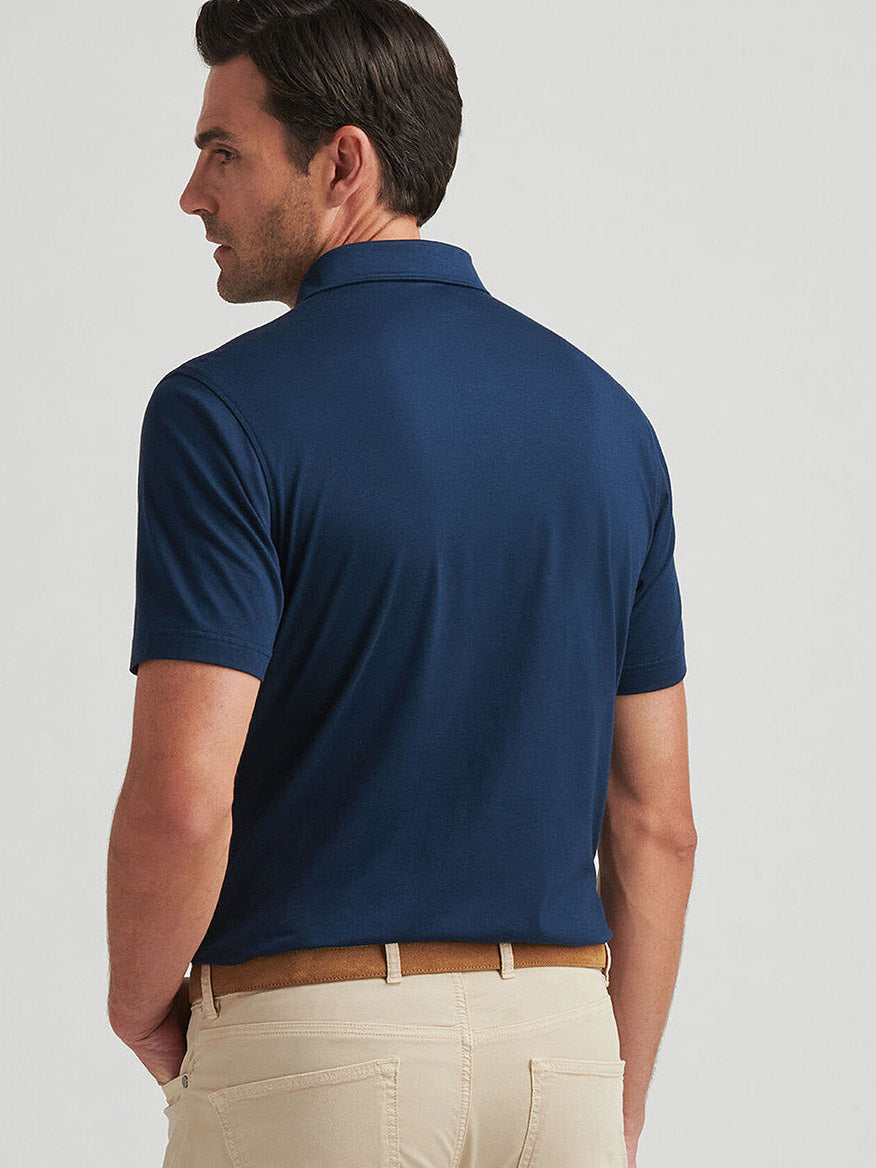 A man is seen from the back wearing a Peter Millar Excursionist Flex Polo in Atlantic Blue, made from a cotton-based jersey knit, and beige pants, delivering comfort with its four-way stretch.