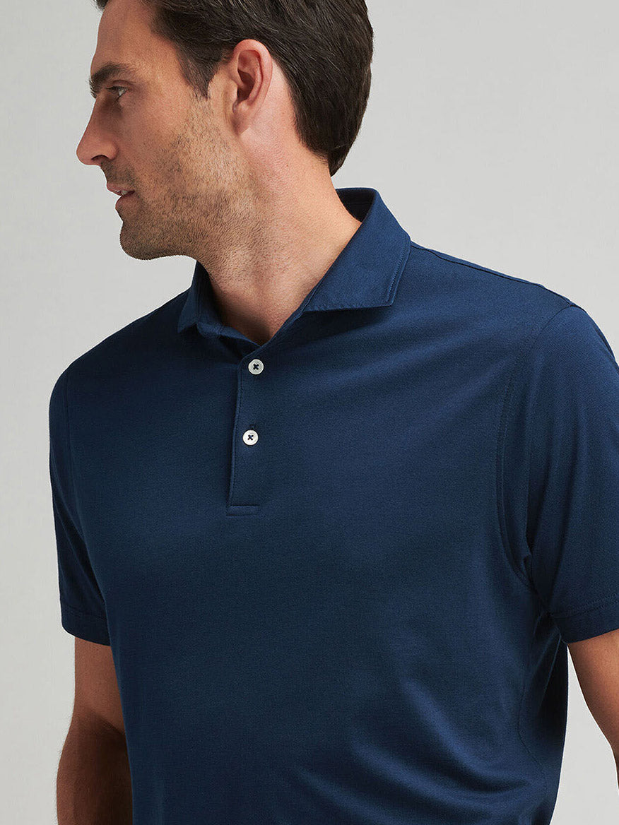 A man in an Atlantic Blue Peter Millar Excursionist Flex Polo, made from a cotton-based jersey knit, glances to the side against a neutral background.