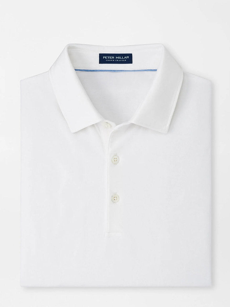 The Peter Millar Excursionist Flex Polo in White is a tailored fit polo shirt with a collar, three buttons, and a label inside the neckline. It features four-way stretch fabric for improved comfort and mobility.