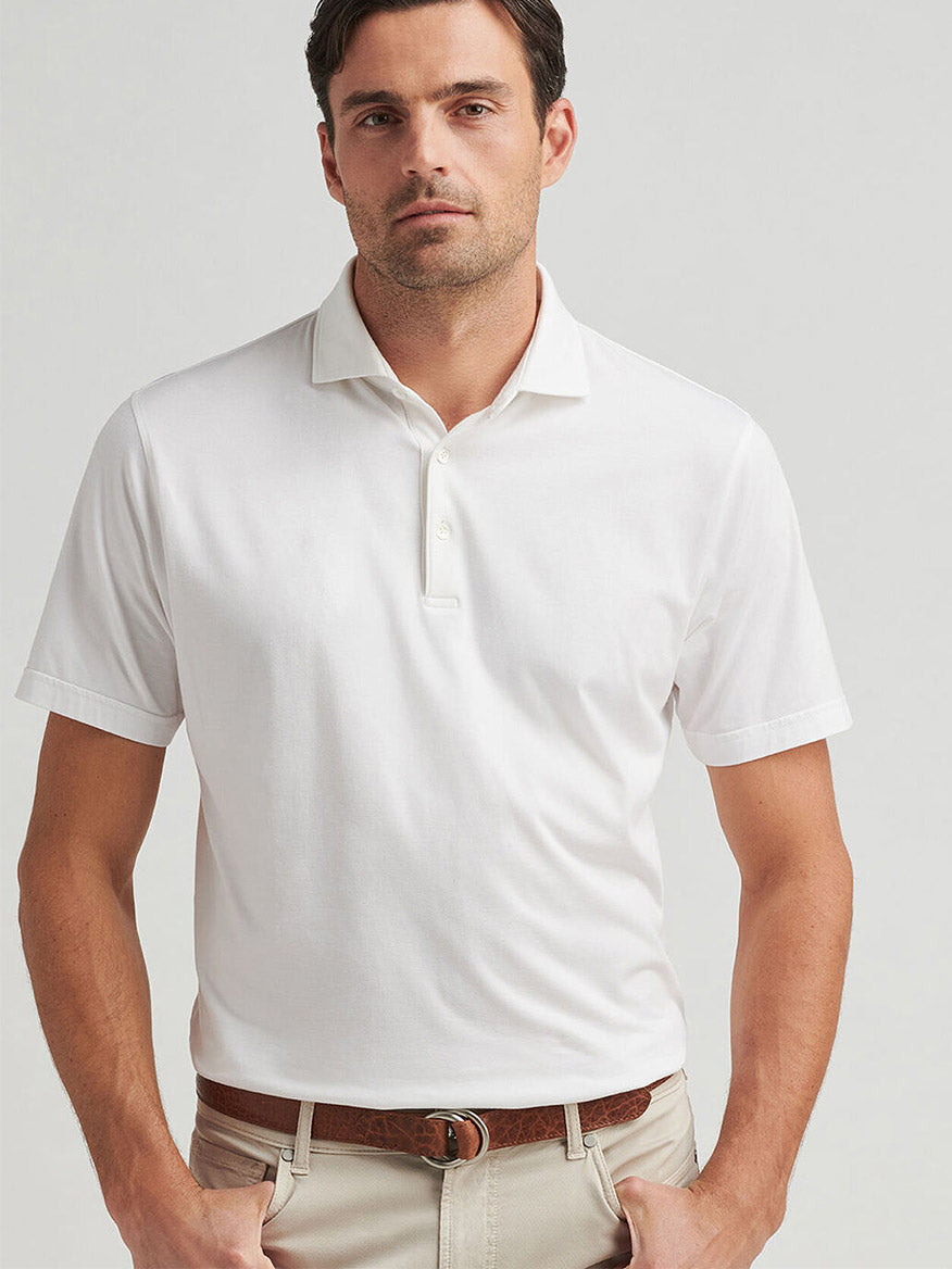 Man in a Peter Millar Excursionist Flex Polo in white and beige pants, standing with hands in pockets.