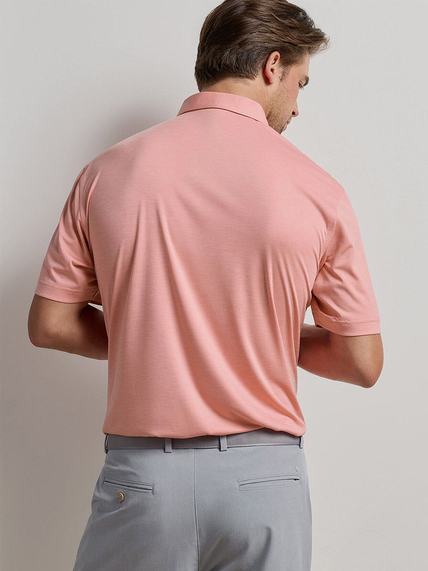 A man wearing a Peter Millar Featherweight Mélange Performance Polo in Venetian Pink with light gray pants faces away from the camera against a plain background.