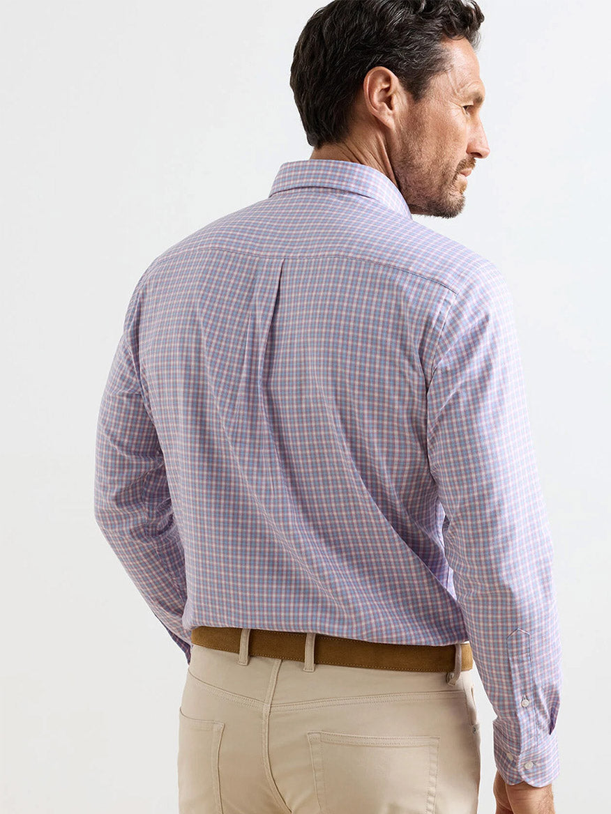 A man stands facing away, wearing a Peter Millar Felix Crown Lite Cotton-Stretch Sport Shirt in Chili Red, tucked into beige pants with a brown belt.