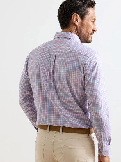 A man stands facing away, wearing a Peter Millar Felix Crown Lite Cotton-Stretch Sport Shirt in Chili Red, tucked into beige pants with a brown belt.