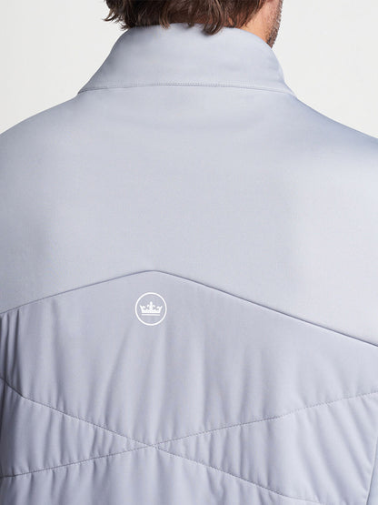 A close-up of a man wearing a Peter Millar Fuse Hybrid Vest in Gale Grey with a branded logo patch on the upper back.