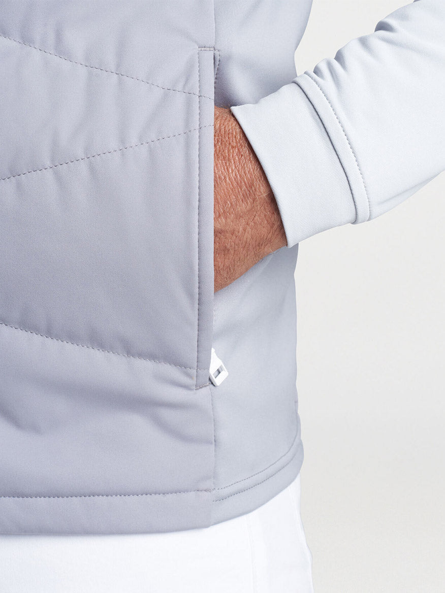 Close-up of a person wearing a Peter Millar Fuse Hybrid Vest in Gale Grey with hand tucked into the pocket.