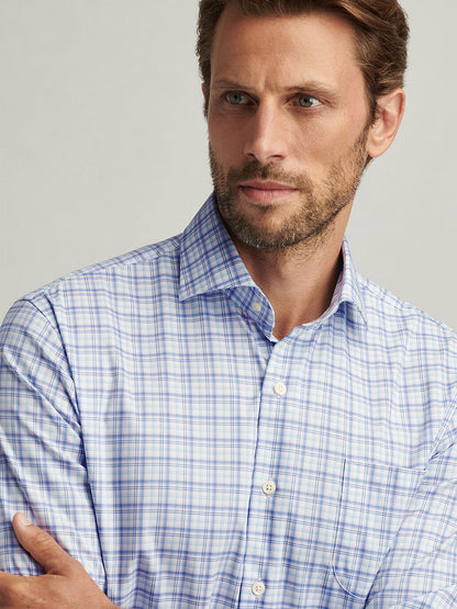 A man with short hair and a beard wears the Peter Millar Garrow Crown Lite Cotton-Stretch Sport Shirt in Blue Freesia, featuring a classic fit and blue and white plaid pattern crafted from easy-care fabric.