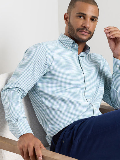 A man sits confidently in a Peter Millar Gregory Performance Twill Sport Shirt in Windsor Blue, made from performance fabric with UPF 50+ protection.
