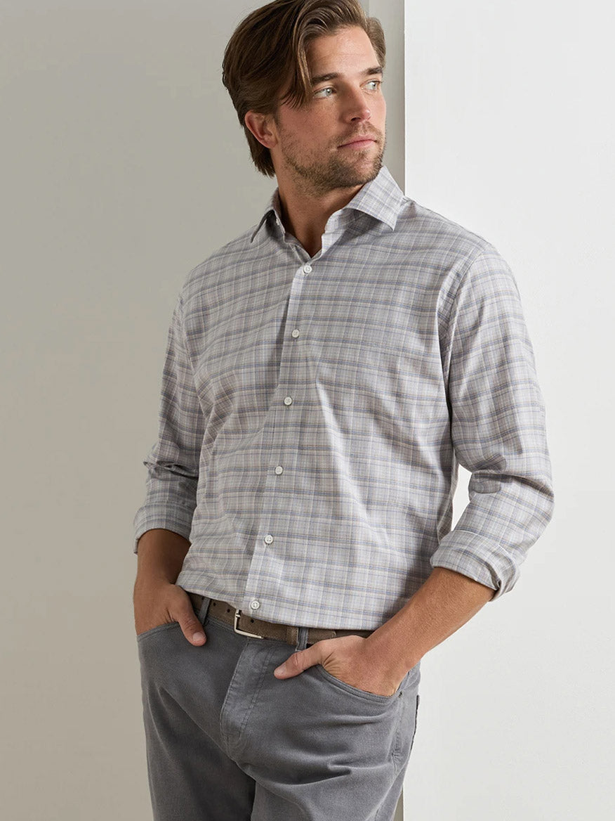 A man stands with his hands in his pockets, wearing the Peter Millar Griffin Crown Soft Twill Sport Shirt in Battleship Grey and grey pants, looking to his right.