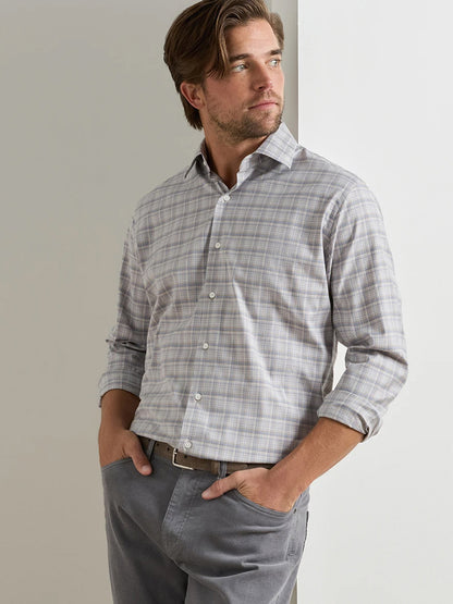 A man stands with his hands in his pockets, wearing the Peter Millar Griffin Crown Soft Twill Sport Shirt in Battleship Grey and grey pants, looking to his right.