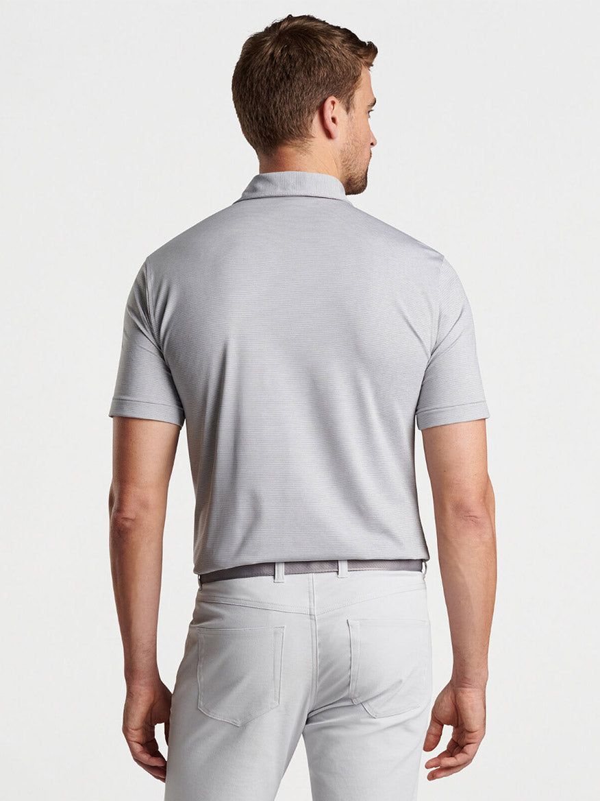 A man wearing a Peter Millar Halford Performance Jersey Polo in Gale Grey and light gray trousers photographed from the back.