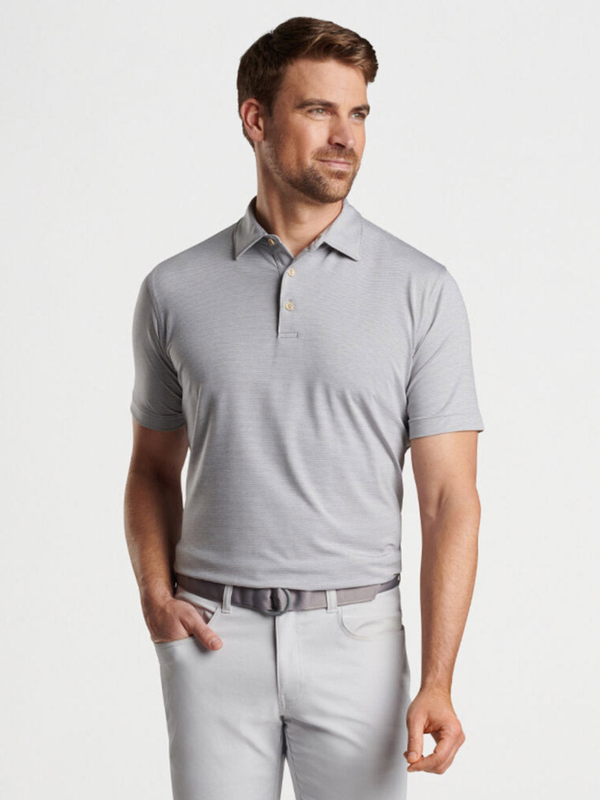 Man in a Peter Millar Halford Performance Jersey Polo in Gale Grey and white pants posing with his hand in his pocket.
