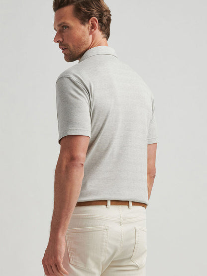 A man wearing the Peter Millar Harris Herringbone Knit Polo in British Grey and beige pants stands facing slightly away, looking to his left.