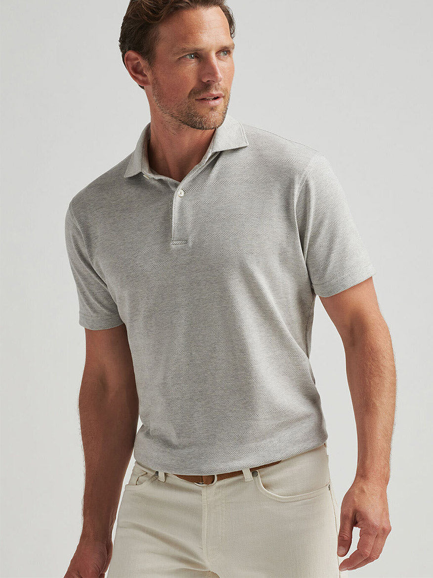 Someone is wearing the Peter Millar Harris Herringbone Knit Polo in British Grey paired with tailored beige pants, standing against a plain background.