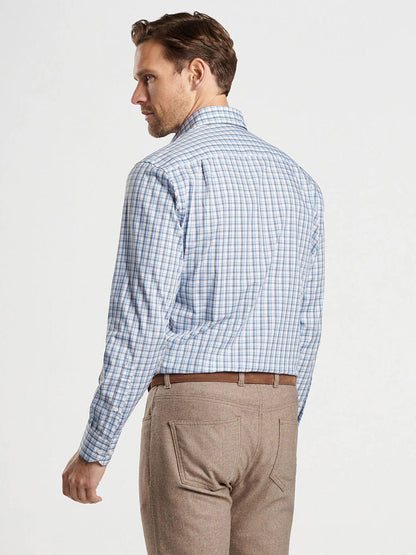 A man with short hair stands facing away, wearing the Peter Millar Howgill Cotton Sport Shirt in Brook Blue and tailored-fit beige pants.