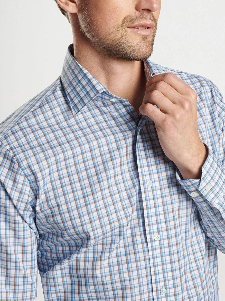 A man wearing the Peter Millar Howgill Cotton Sport Shirt in Brook Blue, expertly crafted from premium cotton yarn, adjusts his collar for a perfectly tailored fit.