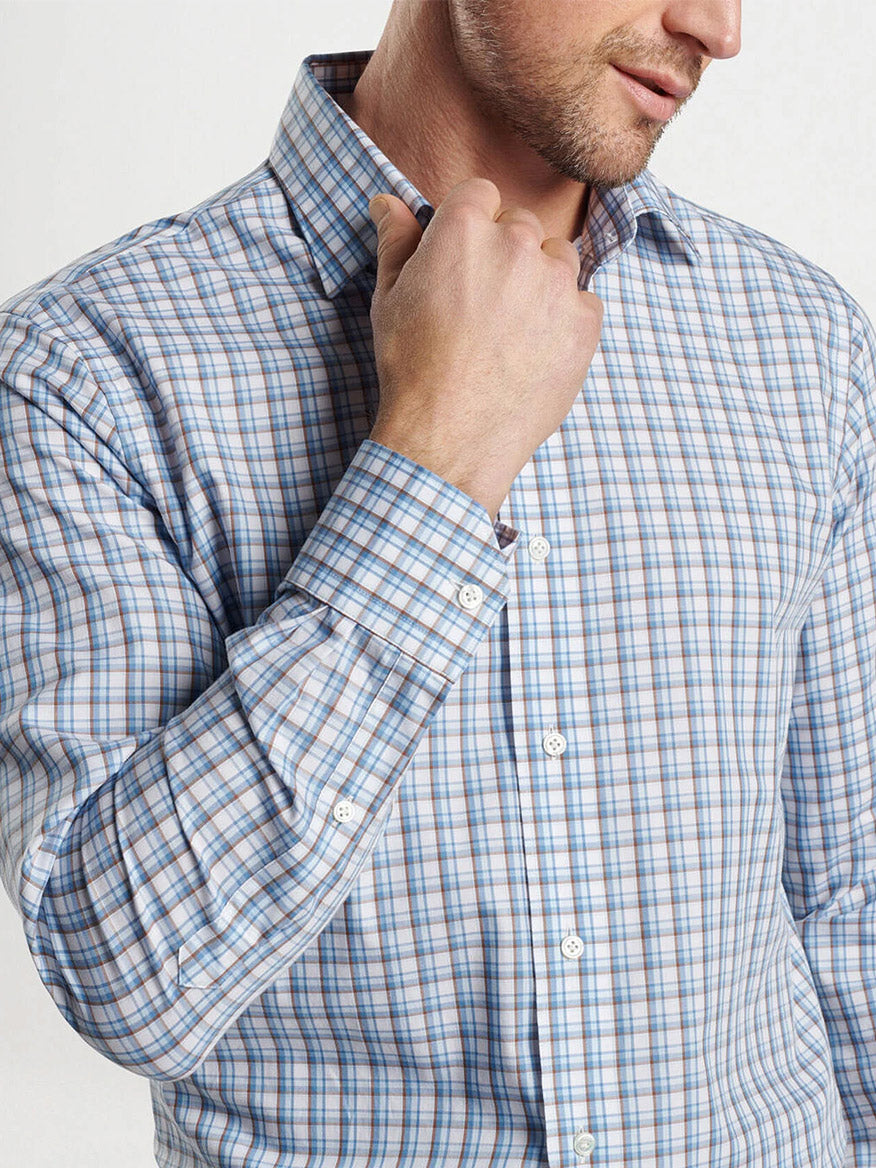 A person sporting the Peter Millar Howgill Cotton Sport Shirt in Brook Blue, made from soft cotton yarn for a tailored fit, adjusts their collar.