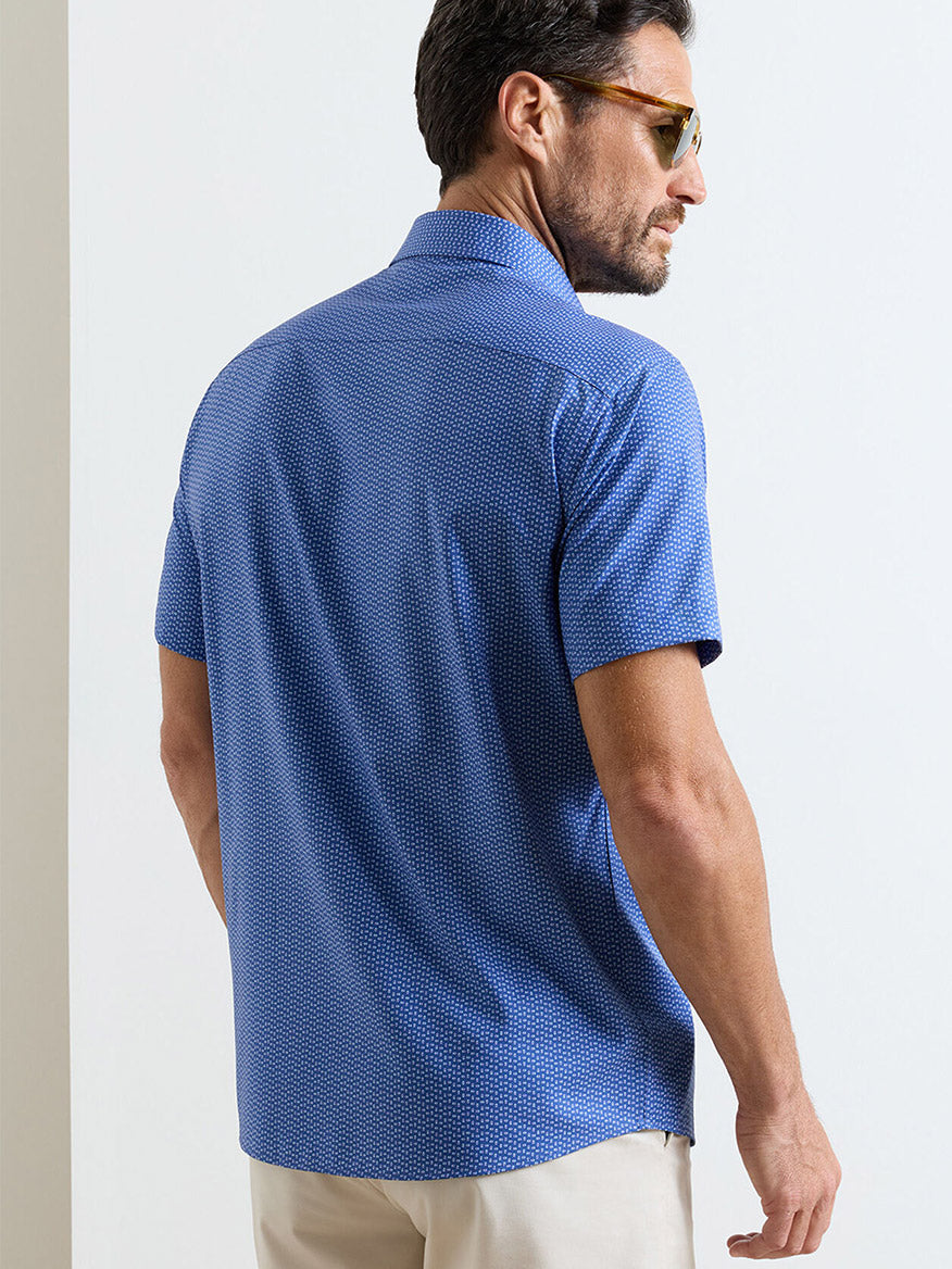 A man in sunglasses and a Peter Millar Jackson Performance Poplin Sport Shirt in Windsor Blue with UPF 50+ sun protection stands facing away from the camera.