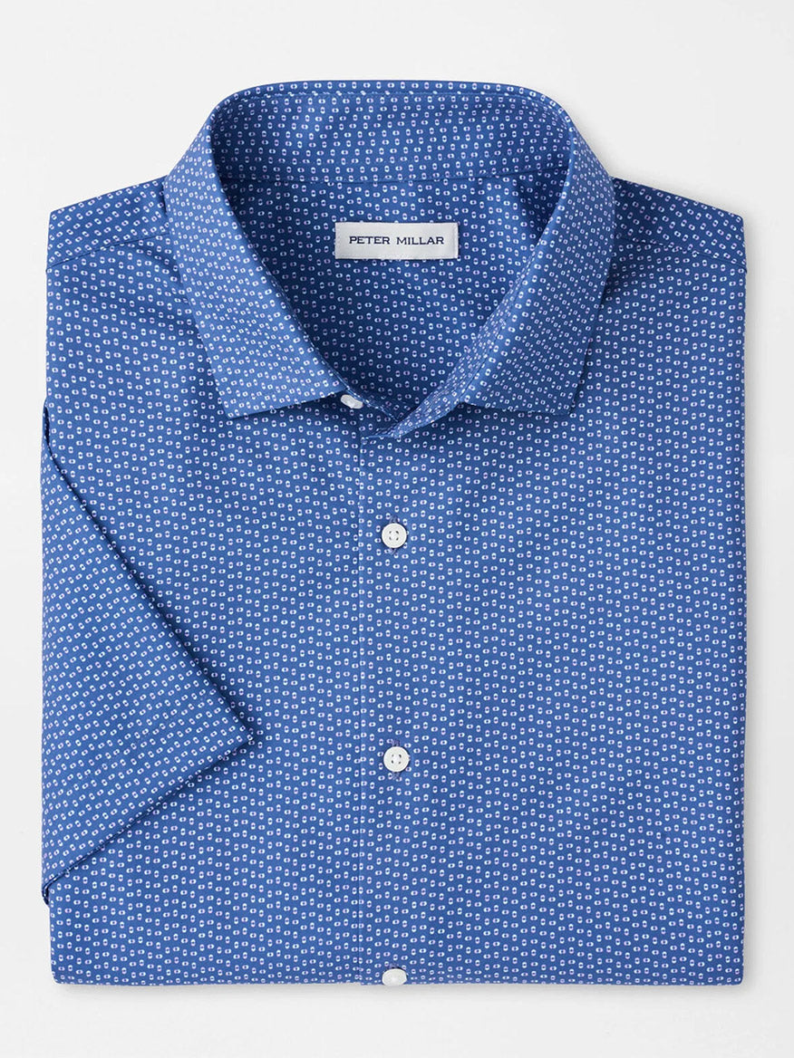 The Peter Millar Jackson Performance Poplin Sport Shirt in Windsor Blue features a small white geometric pattern, UPF 50+ sun protection, and is neatly folded with a "Peter Millar" label.