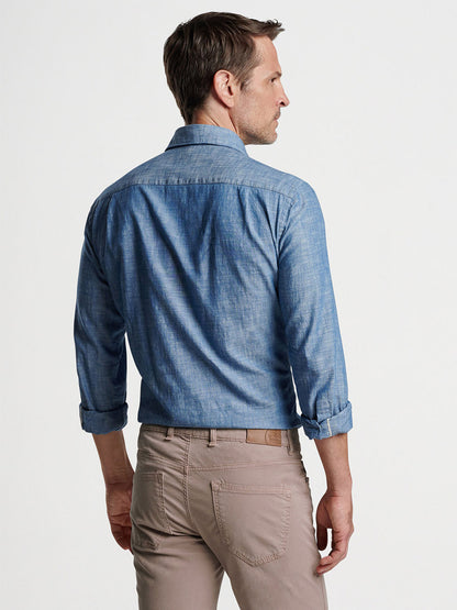 Man wearing a tailored fit, blue denim Peter Millar Japanese Selvedge Sport Shirt in Light Chambray and beige pants viewed from the back.