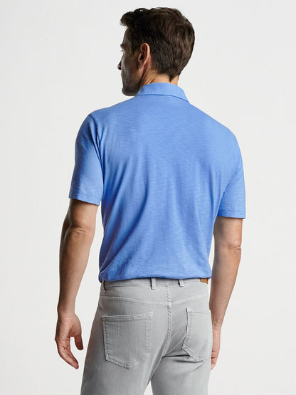 Man viewed from behind wearing a Peter Millar Journeyman Short Sleeve Polo in Regatta Blue and gray pants.