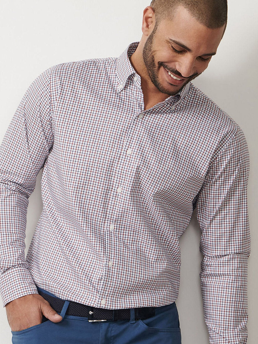 A man with short hair and a beard wears the Peter Millar Julian Crown Lite Cotton-Stretch Shirt in Navy and blue pants, standing against a plain white background, looking down and smiling.