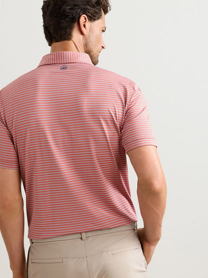 A man stands with his back to the camera wearing a Peter Millar Keynote Performance Jersey Polo in Faded Scarlet and light beige pants.