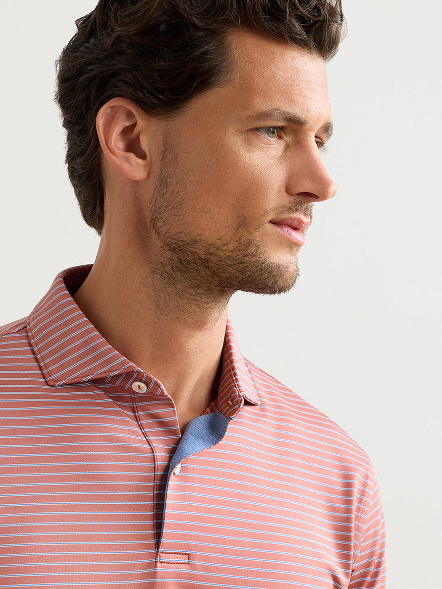 Man with short brown hair and light stubble wearing the Peter Millar Keynote Performance Jersey Polo in Faded Scarlet, looking to his right against a plain background.