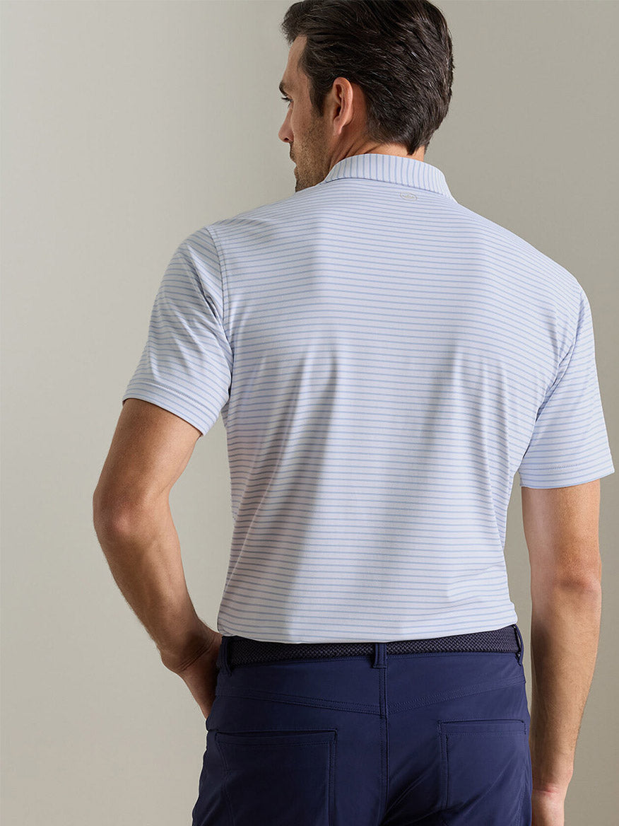 Man wearing the Peter Millar Keynote Performance Jersey Polo in White, featuring light blue and white stripes and UPF 50+ sun protection, with navy pants. Shown from the back against a neutral background.