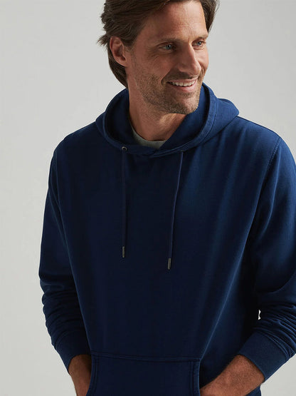 A man wears a Peter Millar Lava Wash Hoodie in Navy, smiling with his hands in the pockets and looking to the side against a plain background.